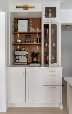 a kitchen with white cabinets and gold trimming on the top shelf is filled with wine glasses