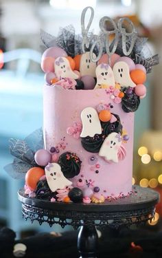 a pink cake decorated with halloween decorations and ghost figures on it's top tier