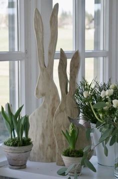 two wooden rabbits sitting next to each other on a window sill with flowers in vases