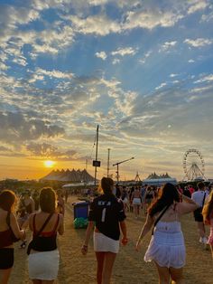 several people are walking around in the sand at an outdoor music festival as the sun sets