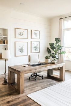 an office with white walls and wood floors, including a desk in the center surrounded by framed pictures