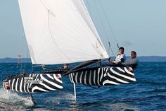 two people riding on the back of a sailboat in the ocean with zebra stripes