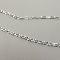 a close up of a silver chain on a gray surface with a black cat in the background