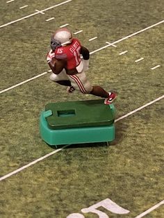 a toy football player running on the field with a green box in front of him