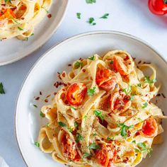 two plates of pasta with tomatoes and parsley