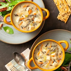 two yellow mugs filled with soup on top of a table next to crackers