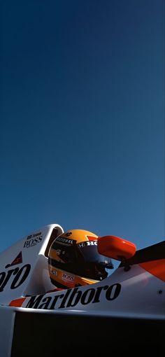 a white and orange race car driving on a track with blue sky in the background