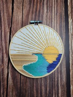 an embroidered sun and ocean scene on a wooden surface with two pins in the middle