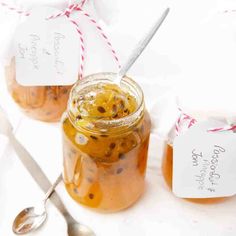 two jars filled with food sitting on top of a white table next to spoons