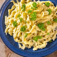 a blue plate topped with macaroni and cheese covered in parsley on top of a wooden table