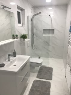 a bathroom with white walls and flooring has a toilet, sink, shower, and rugs