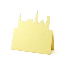 a piece of yellow paper with a city skyline cut out on it's side