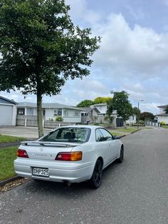 a white car parked on the side of a road next to a tree and houses