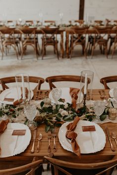 a wooden table topped with white plates and silverware