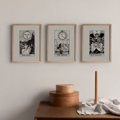 three framed tarot cards hang on the wall above a wooden table