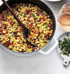 a pot filled with corn and vegetables next to two glasses of wine on a table