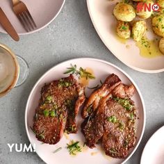 two white plates topped with meat and potatoes next to glasses of wine on a table