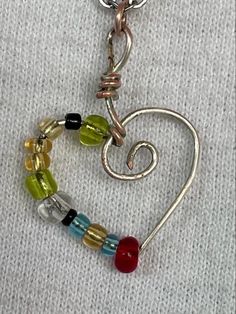 a heart shaped pendant with beads and charms on it's side, hanging from a silver chain