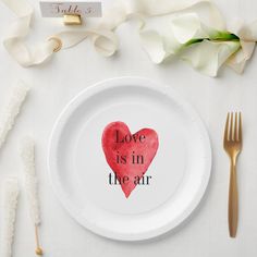 a white plate topped with a red heart on top of a table next to utensils