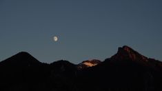 the moon is setting over some mountains