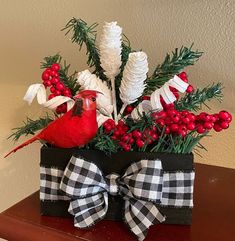 a red bird sitting on top of a black box filled with berries and greenery