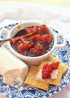 a blue and white plate topped with crackers and fruit jelly next to a piece of cheese