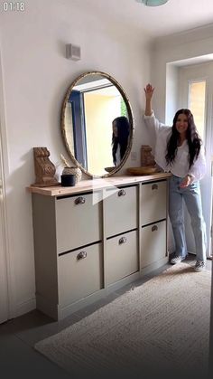 a woman standing in front of a dresser with a mirror on it's side