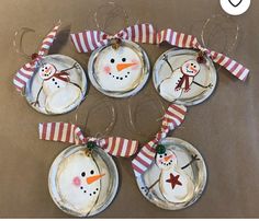 four snowman ornaments hanging from the side of a table with red and white striped ribbon