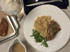 a white plate topped with pasta and meat next to a glass of wine on top of a table