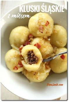 a white bowl filled with dumplings covered in cheese and bacon next to a fork