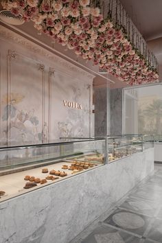 a display case filled with lots of pastries in front of a wall covered with flowers