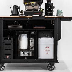 a black cart with various items on it and a coffee pot sitting on top of the cart