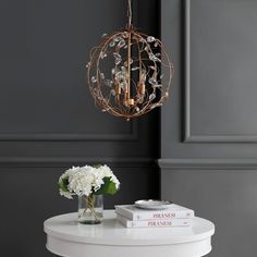 a white table topped with a vase filled with flowers next to two books and a chandelier