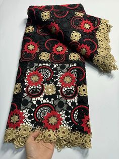 a hand is holding up a black and red scarf with gold lace on the edges