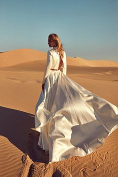 a woman standing in the desert wearing a long white dress and high heeled shoes