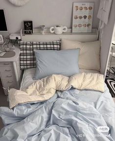 an unmade bed with blue sheets and pillows in a small room next to a dresser