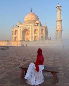 a woman sitting on a bench in front of a building with a red scarf around her head