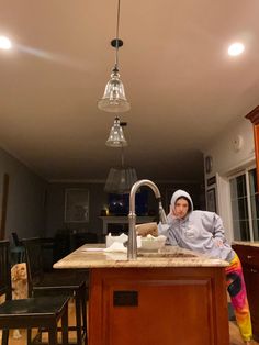 a woman sitting at a kitchen sink in the middle of a room with lights on