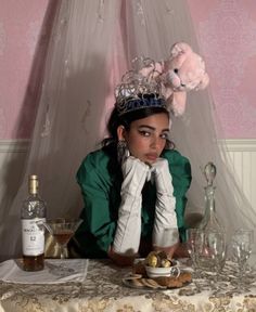 a woman sitting at a table wearing a tiara and holding her hands to her face