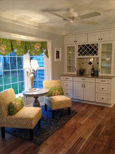 a living room with two chairs and a table in front of a window that has green curtains on it