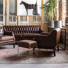 a living room with brown leather furniture and large painting on the wall above it's fireplace