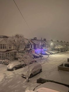 a snowy street with cars parked on the side and houses in the background at night