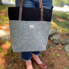 a woman holding a gray and black tote bag in her hands while standing on the ground