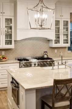 a kitchen with white cabinets and marble counter tops, an island in the middle is surrounded by two chairs