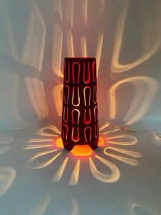 a red vase sitting on top of a white table next to a light that is reflecting off the wall