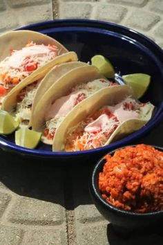 three tacos in a blue bowl next to some red rice and lime wedges