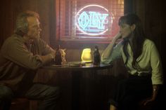 a man and woman sitting at a table in front of a neon sign with the word time bomb on it