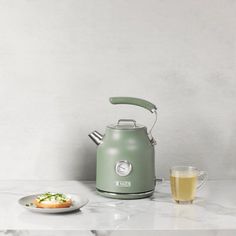 a green kettle sitting on top of a counter next to a plate of food