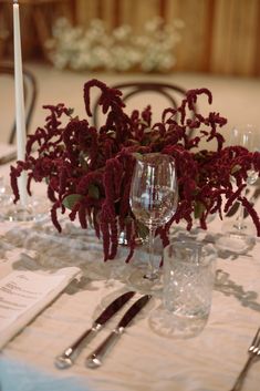 the table is set with silverware and red flowers in vases on top of it