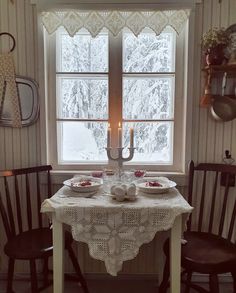 the table is set for two with plates and cups on it, in front of a window